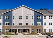 Thumbnail 11 of 22 - A large building with a blue and white exterior and a covered walkway in front.