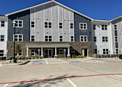 Thumbnail 2 of 22 - A large building with a parking lot in front.