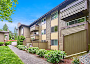 Thumbnail 12 of 19 - Exterior view of personal patios or balconies, manicured grounds and building, and blue skies in the background at Heritage Grove, Renton, WA.