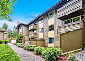 Thumbnail 13 of 19 - Exterior view of personal patios or balconies, manicured grounds and building, and blue skies in the background at Heritage Grove, Renton, WA.