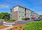 Thumbnail 6 of 14 - Exterior apartments with green bushes and trees and on-site community parking.