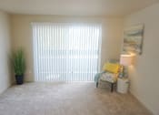 Thumbnail 19 of 19 - a living room with a large sliding glass door, beige carpet and a chair at Heritage Grove Apartments in Renton, WA