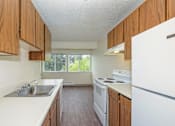 Thumbnail 1 of 14 - Double galley kitchen, wood cabinet storage, white countertops, and appliances. Full-size fridge, dishwasher, oven, stove top.