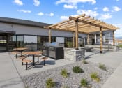 Thumbnail 12 of 36 - a patio with picnic tables and a grill in front of a building at Yellowstone Landing, Belgrade, MT, 59714