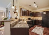 Thumbnail 68 of 84 - a kitchen with espresso color cabinets, granite countertops, designer lighting fixtures and black appliances  at Grand Villas Apartments, Katy