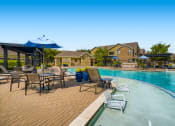 Thumbnail 49 of 84 - a swimming pool with chairs and umbrellas next to club house at Grand Villas Apartments, Katy, Texas