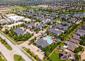 Thumbnail 37 of 47 - A bird's eye view of a residential neighborhood with houses, a swimming pool, and a school at Avenues at Shadow Creek Ranch Apartments, Pearland, Texas
