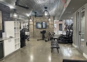 Thumbnail 23 of 63 - a gym with weights machines and a tv on a brick wall at Edge 35, Indianapolis
