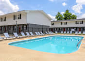 Thumbnail 21 of 43 - A large swimming pool with lounge chairs in front of a white building at Spring Creek Townhomes Apartments, Springfield, Illinois