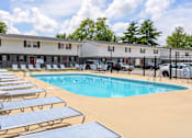 Thumbnail 22 of 43 - A pool surrounded by sun loungers and a building in the background at Spring Creek Townhomes Apartments, Illinois
