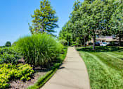 Thumbnail 35 of 53 - A walkway in a park with green grass and trees at Sovereign at Overland Park Apartments, Overland Park, KS 66213