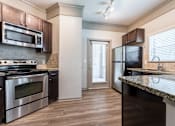 Thumbnail 39 of 40 - A kitchen with dark brown cabinets and stainless steel appliances at Waterstone at Cinco Ranch Apartments, Texas, 77450