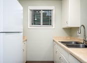 Thumbnail 13 of 22 - A kitchen with a white refrigerator and a window with blinds.