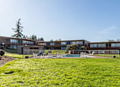 Thumbnail 16 of 26 - A large grassy area in front of a building with a pool table and chairs.