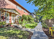 Thumbnail 19 of 20 - A red building with a white door and windows is surrounded by greenery and a stone pathway.