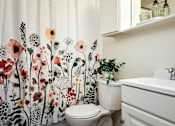 Thumbnail 26 of 26 - A white toilet sits next to a sink in a bathroom with a floral shower curtain.