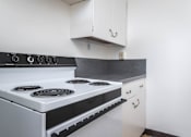 Thumbnail 17 of 52 - A white stove with a black top is in a kitchen with white cabinets.