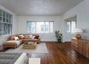 Thumbnail 1 of 52 - A living room with a grey sofa, a wooden coffee table, and a potted plant.