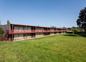 Thumbnail 12 of 26 - A long building with a red roof and a green lawn in front.