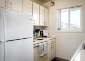 Thumbnail 6 of 26 - A white refrigerator stands in a kitchen with white cabinets and a window.