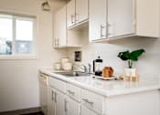 Thumbnail 5 of 26 - A kitchen with white cabinets and a white countertop with a sink and a plant on it.