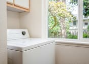 Thumbnail 25 of 26 - A white washing machine sits in a small laundry room.