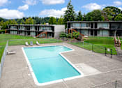 Thumbnail 21 of 26 - A large swimming pool in a fenced in area with a building in the background.