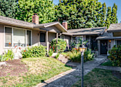 Thumbnail 8 of 24 - A house with a grey roof and a black door is surrounded by greenery.