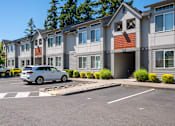 Thumbnail 4 of 13 - A white car is parked in a parking lot in front of a building.