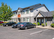 Thumbnail 6 of 13 - A parking lot in front of a building with cars parked.