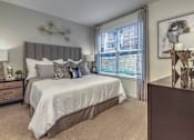 Thumbnail 1 of 11 - A bedroom with a large bed and a nightstand with a plant on it at Crabtree Lakeside Apartments, Raleigh, NC, 27612