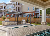 Thumbnail 9 of 11 - A patio with a grill and chairs is in front of a building at Crabtree Lakeside Apartments, Raleigh, 27612