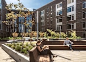 Thumbnail 5 of 36 - Person sitting reading on bench in sunlit courtyard