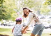Thumbnail 17 of 45 - Child riding bike while woman helps looking back at camera