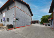 Thumbnail 16 of 20 - a parking lot in front of a gray building with a red curb at The Crossings at Montrose Apartments, San Antonio