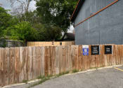 Thumbnail 3 of 20 - a wooden fence with signs on it in front of a building at The Crossings at Montrose Apartments, Texas