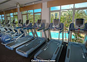 Thumbnail 52 of 57 - A row of treadmills in a gym with a pool in the background at Purl Apartments, San Diego, CA, 92108