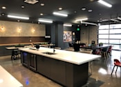 Thumbnail 36 of 57 - A modern kitchen with a white counter and black cabinets at Purl Apartments, San Diego, California