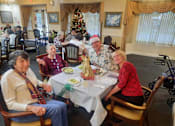Thumbnail 53 of 59 - A group of people are sitting around a table in a room with a Christmas tree in the background  at Savannah Grand of Sarasota, Sarasota, Florida