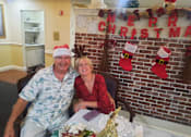 Thumbnail 56 of 59 - A man and woman sitting in front of a Merry Christmas sign  at Savannah Grand of Sarasota, Sarasota, 34238.