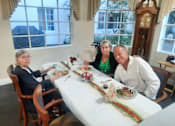 Thumbnail 58 of 59 - Three people are sitting at a table with a white tablecloth and a long centerpiece. at Savannah Grand of Sarasota, Sarasota, 34238.