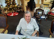 Thumbnail 59 of 59 - A woman in a striped shirt sits at a table with a Christmas tree in the background  at Savannah Grand of Sarasota, Sarasota, 34238.