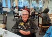 Thumbnail 52 of 59 - A man in a wheelchair sits at a table with a plate of food in front of him  at Savannah Grand of Sarasota, Sarasota, 34238.