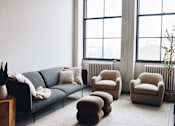 Thumbnail 2 of 10 - A living room with a grey couch, two armchairs, a coffee table, and a plant.