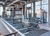 Thumbnail 9 of 19 - A gym with a variety of equipment including a bench, weights, and a TRX system.