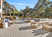 Thumbnail 17 of 24 - A patio with a grey floor and white furniture surrounded by trees.