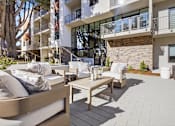 Thumbnail 8 of 24 - A patio with a couch, table, and chairs in front of a building.