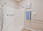 Thumbnail 25 of 25 - A white bathtub with a shower head and a blue towel hanging on the wall.