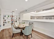 Thumbnail 11 of 25 - A white room with a table and chairs and a bookshelf.