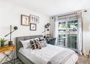 Thumbnail 101 of 111 - A bedroom with a bed, a nightstand, and a window with a view of a balcony.